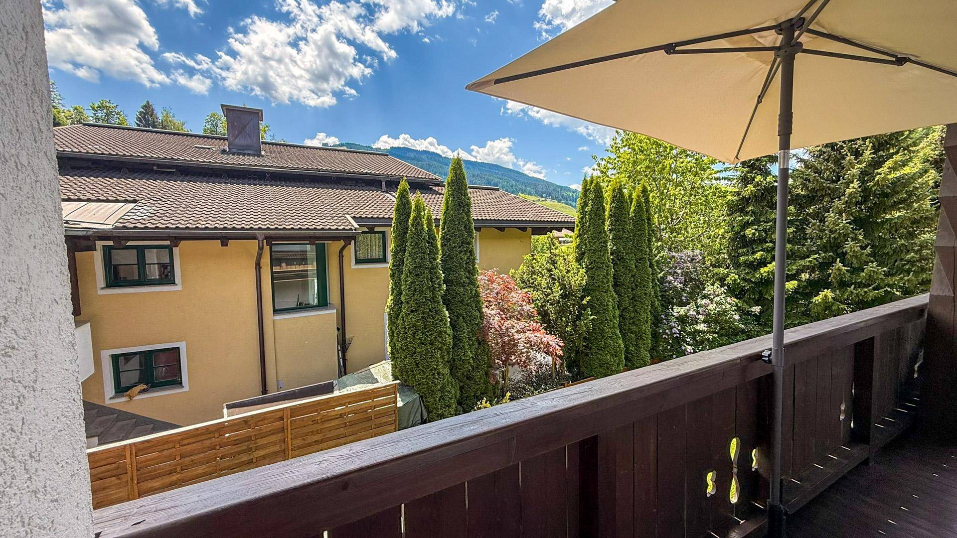 Sonniger Balkon mit Sonnenschirm und Blick auf die umliegende Natur und Berge.