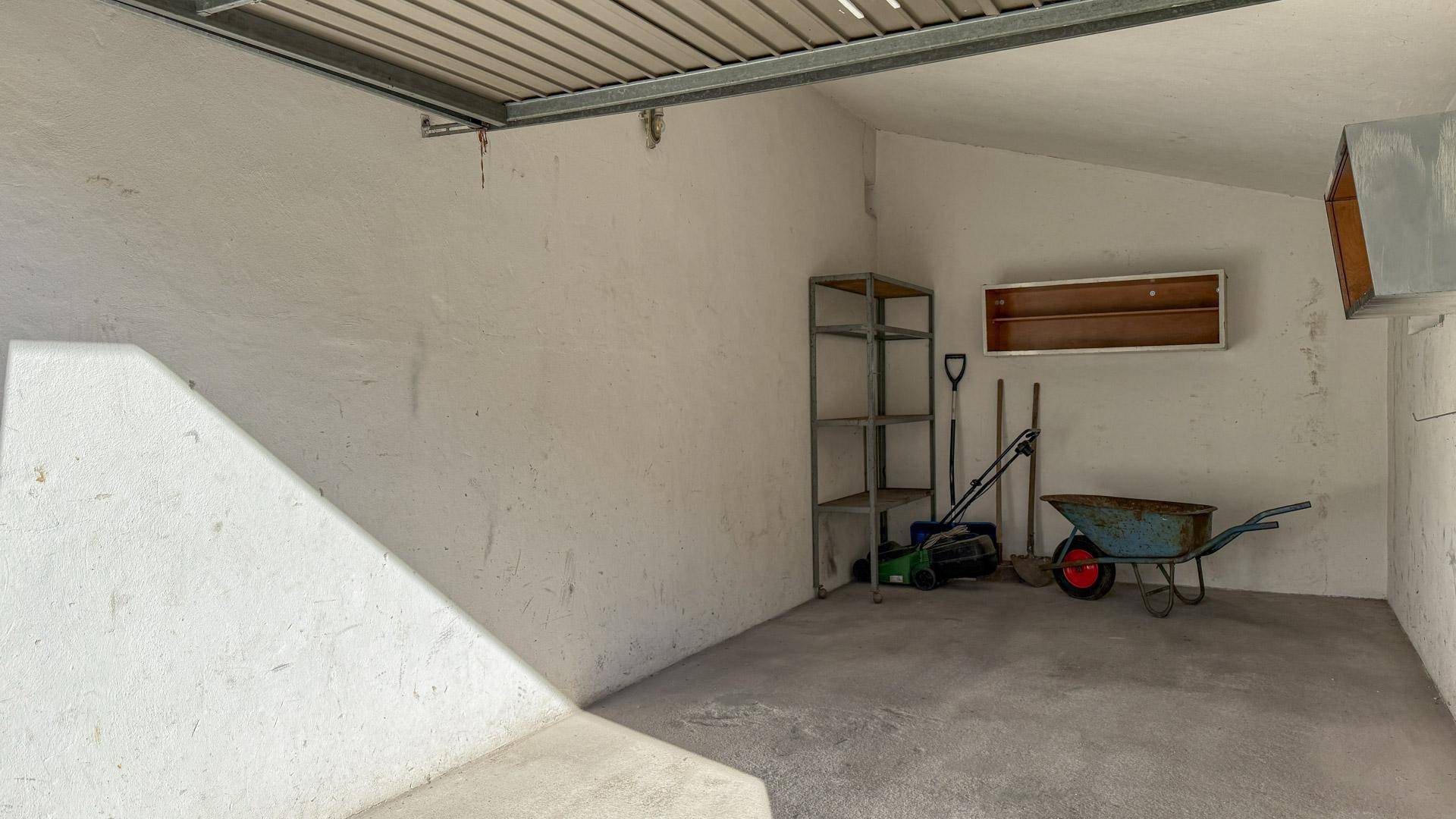 Innenansicht der Garage mit Regalen, Schaufel und Schubkarre für Gartenarbeiten und Lagerung.