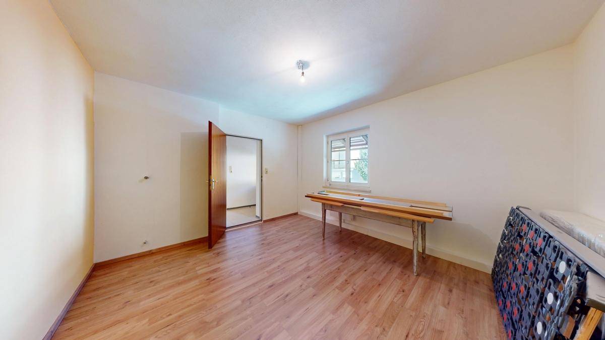 Leeres Zimmer mit Holzboden, einem Fenster und einer einfachen Arbeitsfläche, bereit zur Einrichtung.