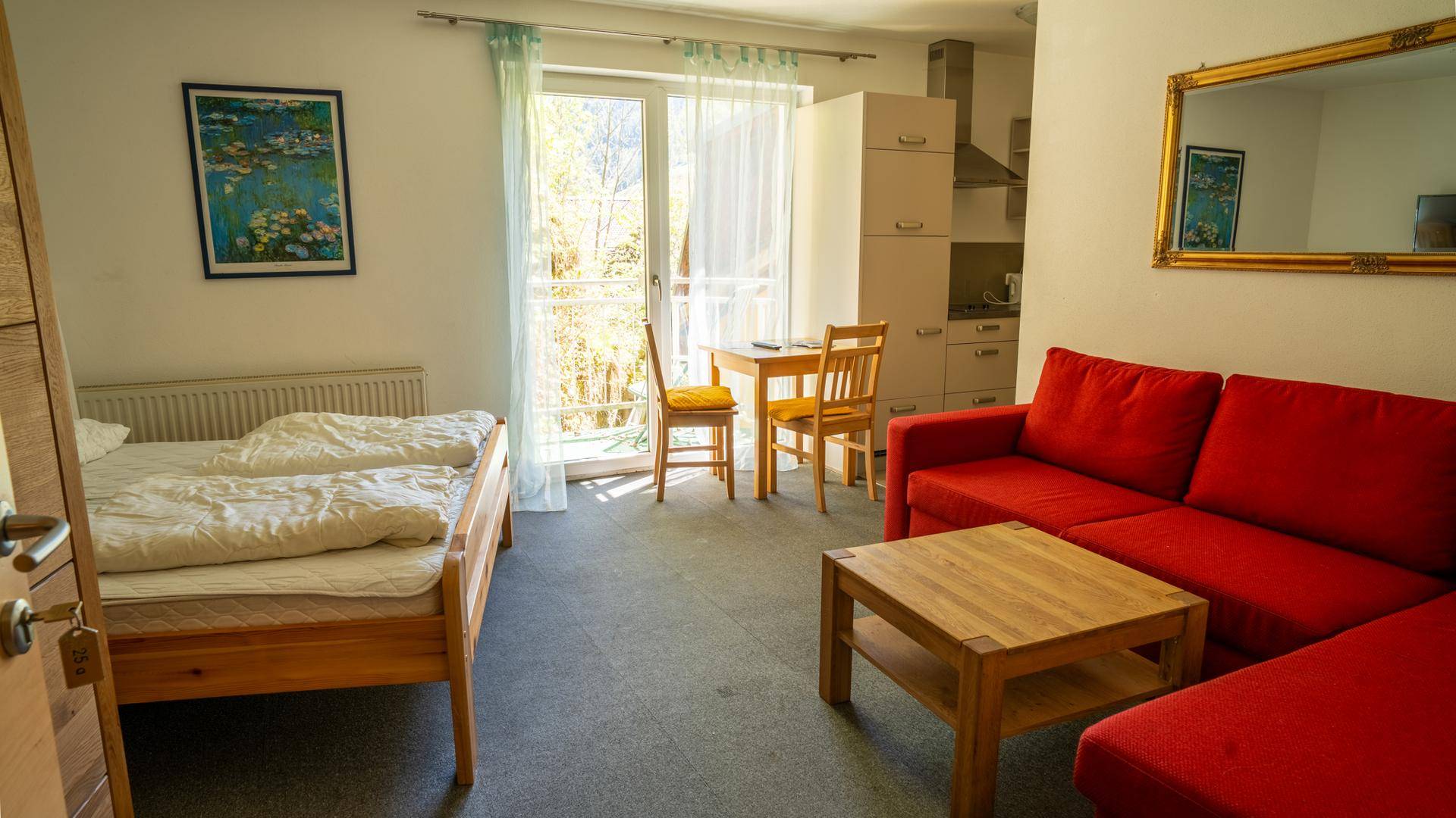 Helles Schlafzimmer mit Doppelbett, rotem Sofa und Balkonzugang.