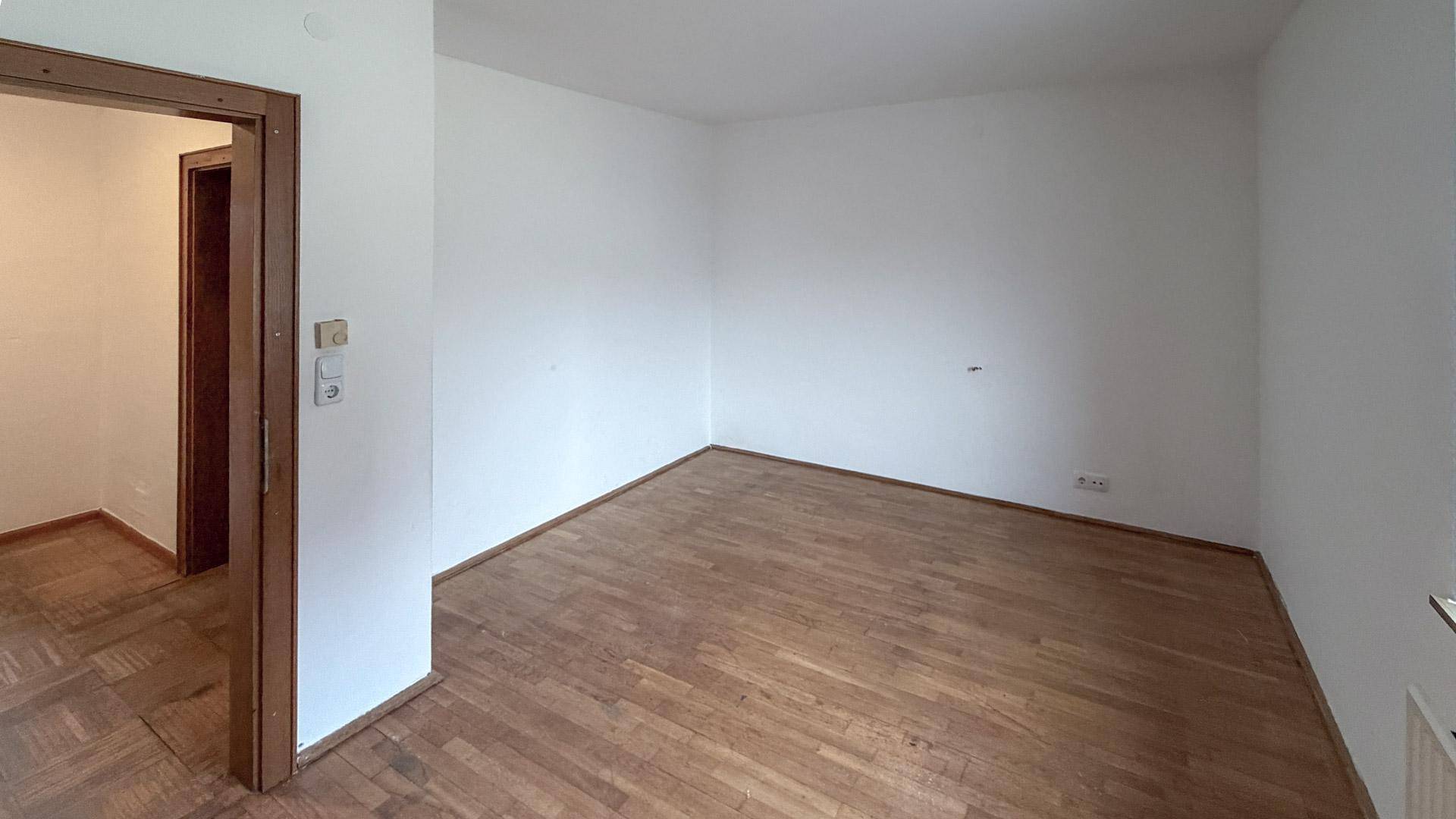 Leeres Wohnzimmer mit Parkettboden und weißen Wänden, bereit zur Gestaltung.