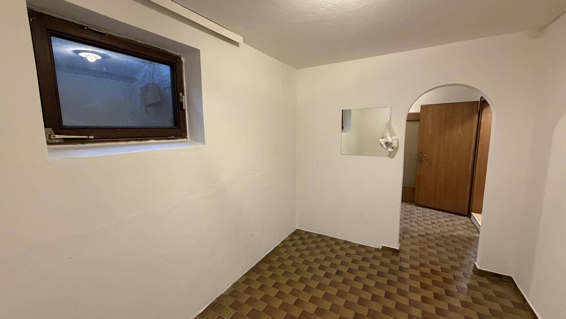 Kellerraum mit Fliesenboden und kleinem Fenster, ideal als Abstellraum.
