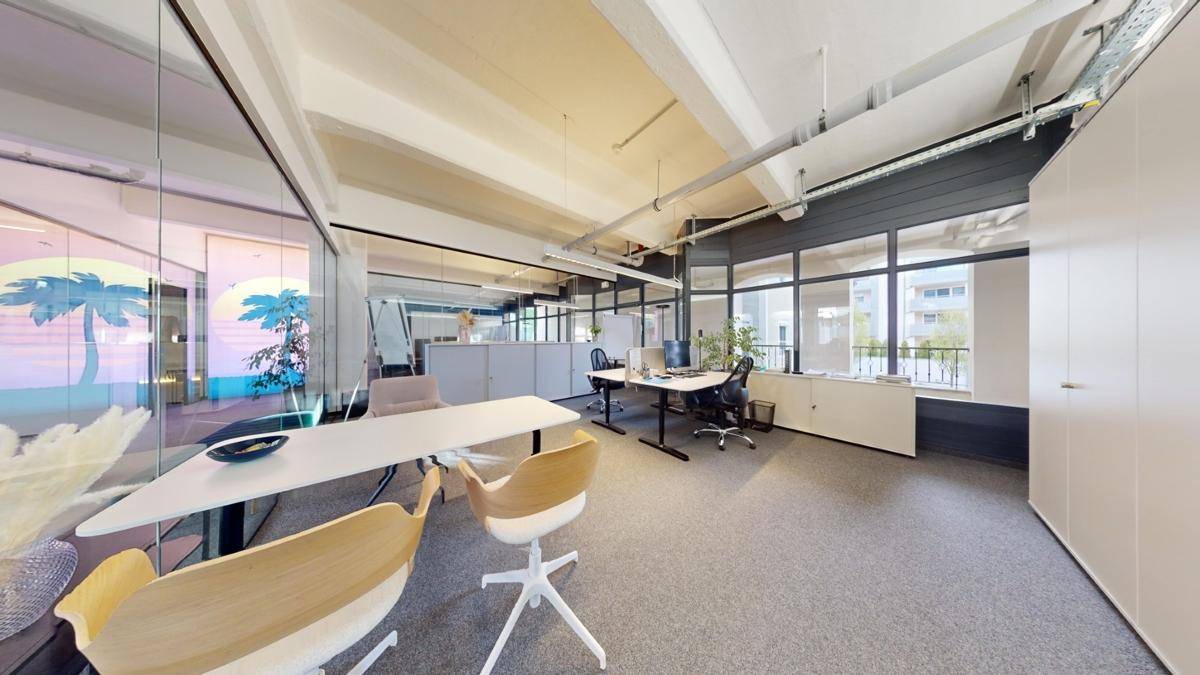 Großzügiges Büro mit mehreren Arbeitsplätzen, großen Fenstern und einer modernen Einrichtung, die eine produktive Umgebung schafft.