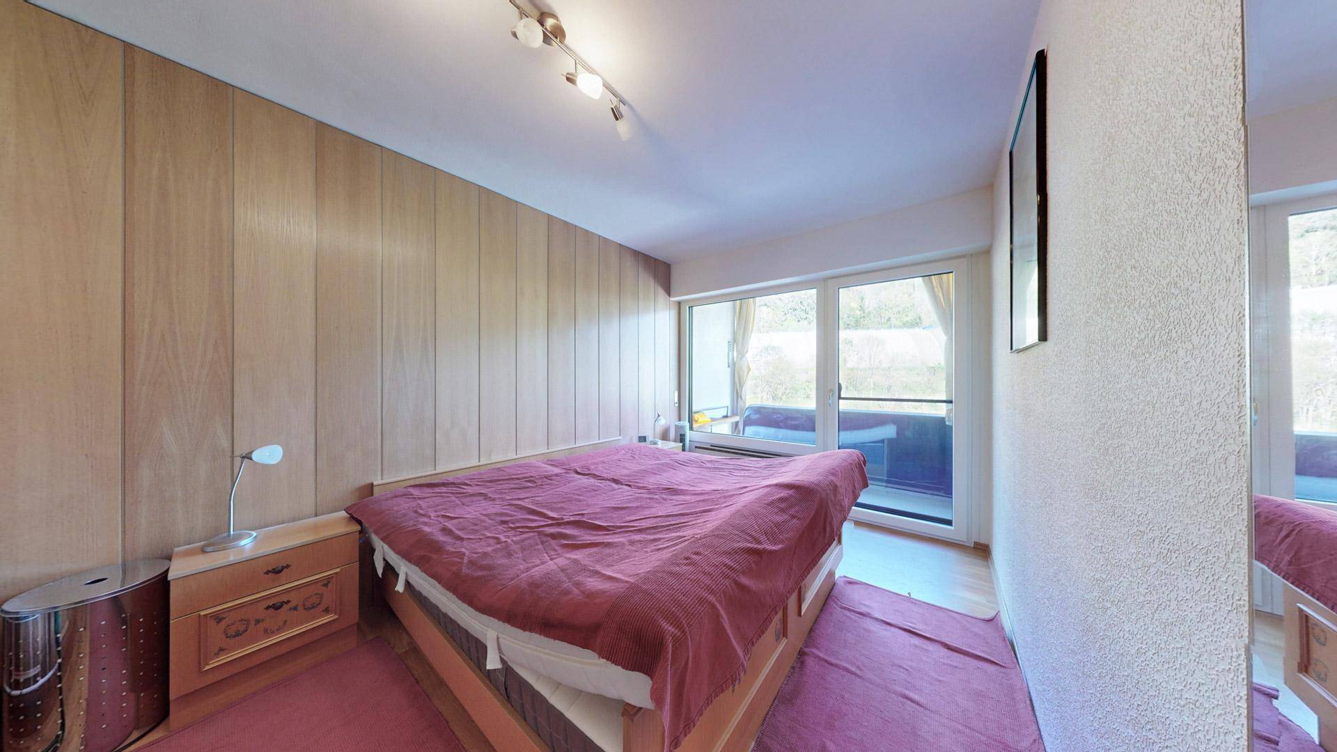 Schlafzimmer mit Doppelbett, Holzvertäfelung und Zugang zu einem Balkon.