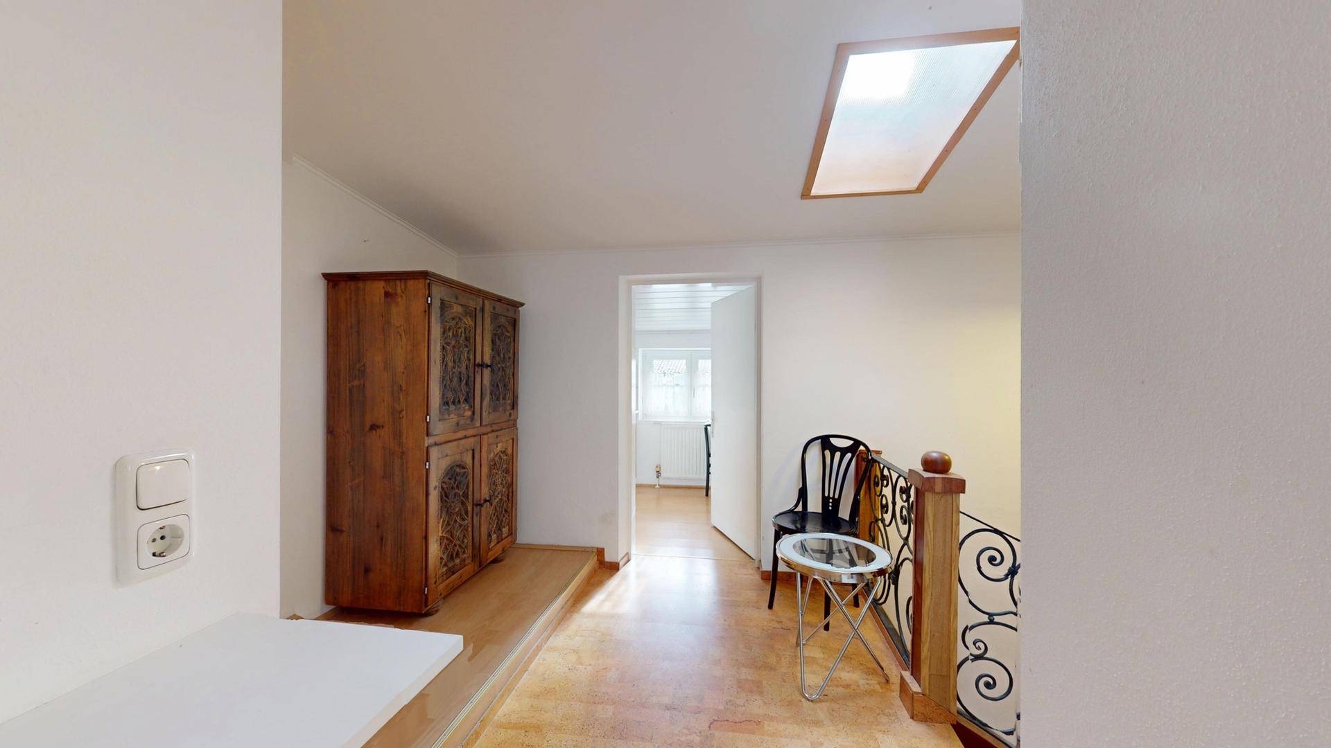 Heller Flur im Obergeschoss mit Dachfenster, Holzschrank und schmiedeeisernem Geländer.