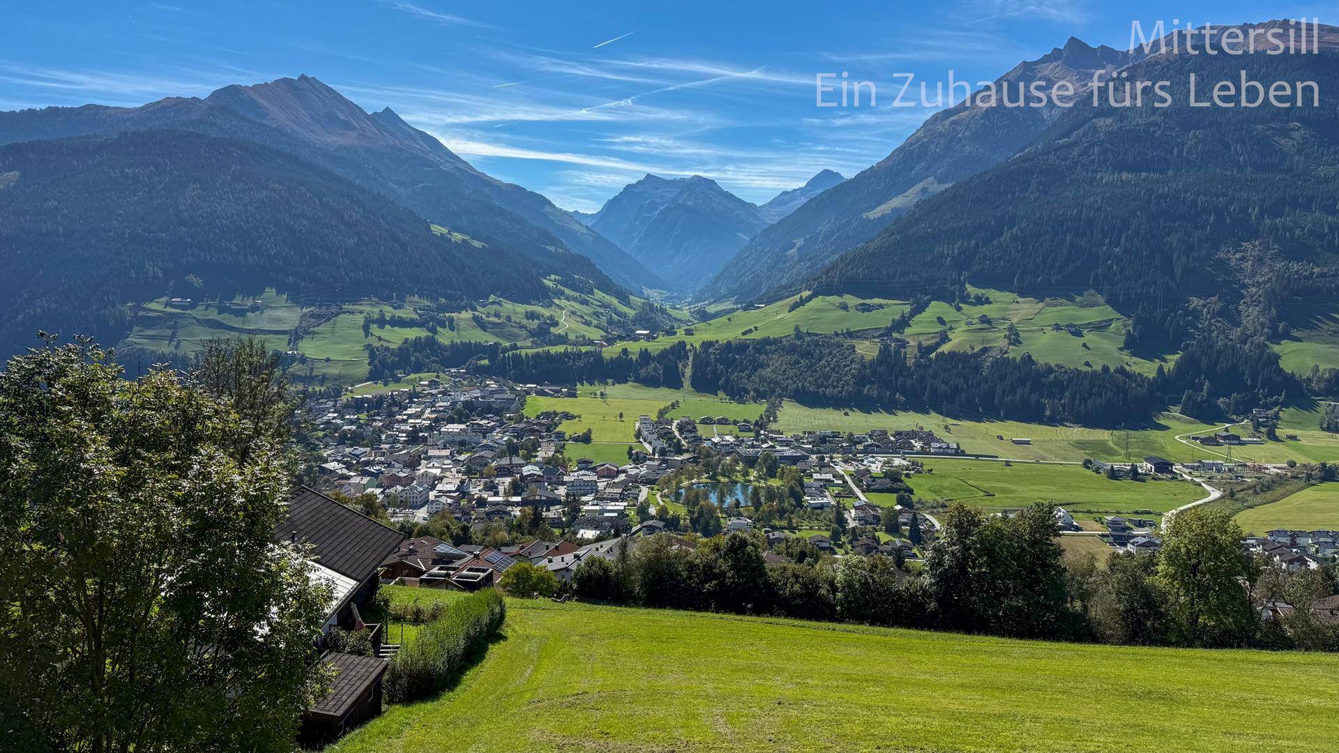 Panoramablick auf das Tal mit einem Dorf und majestätischen Bergen im Hintergrund.