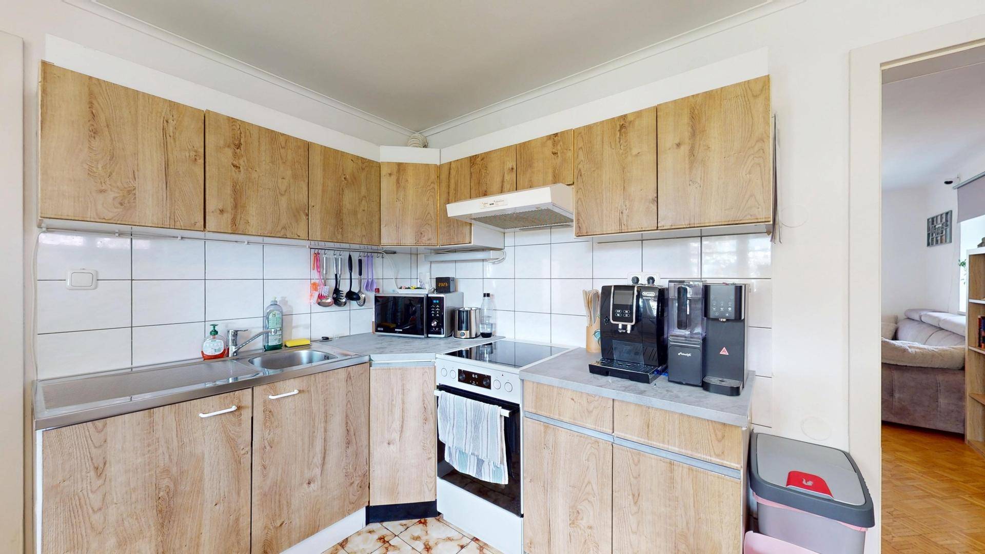 Kleine Küche mit Holzdekorfronten, Elektroherd und Blick in den Wohnbereich.