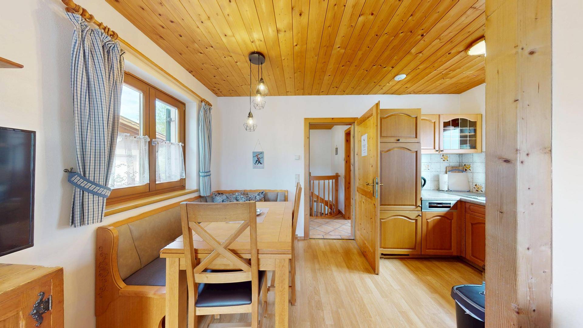 Essbereich mit Holztisch und Sitzbank, angrenzend an eine kleine Küche mit Holzschränken.