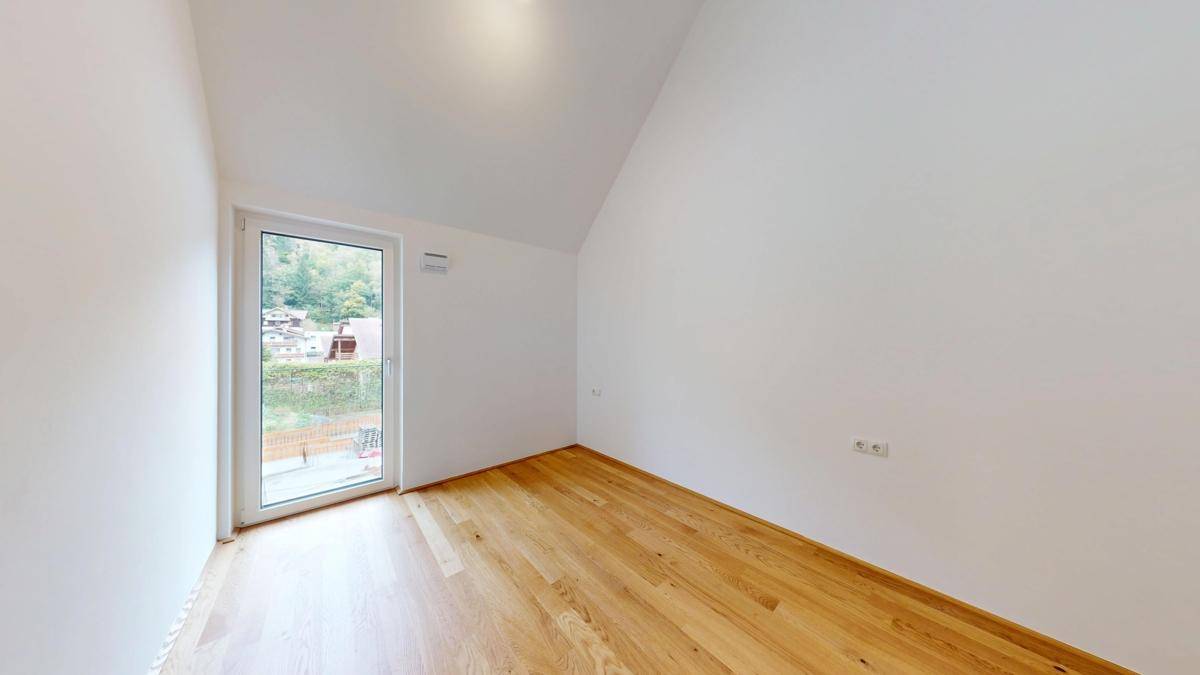 Helles Zimmer mit Holzboden und einer Tür, die auf einen kleinen Balkon führt.