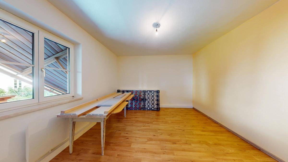 Helles Zimmer mit Holzboden und großem Fenster, das viel Tageslicht hereinlässt, ideal für ein Schlafzimmer.