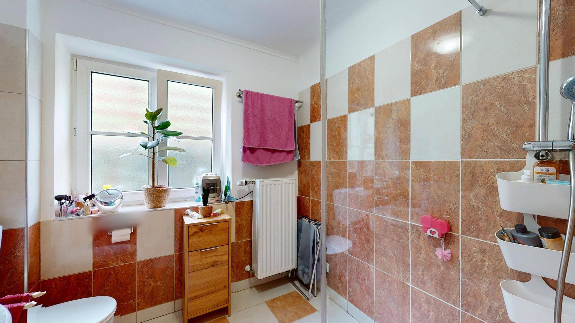 Badezimmer mit Dusche, Fenster und braun-weißen Fliesen im Schachbrettmuster.