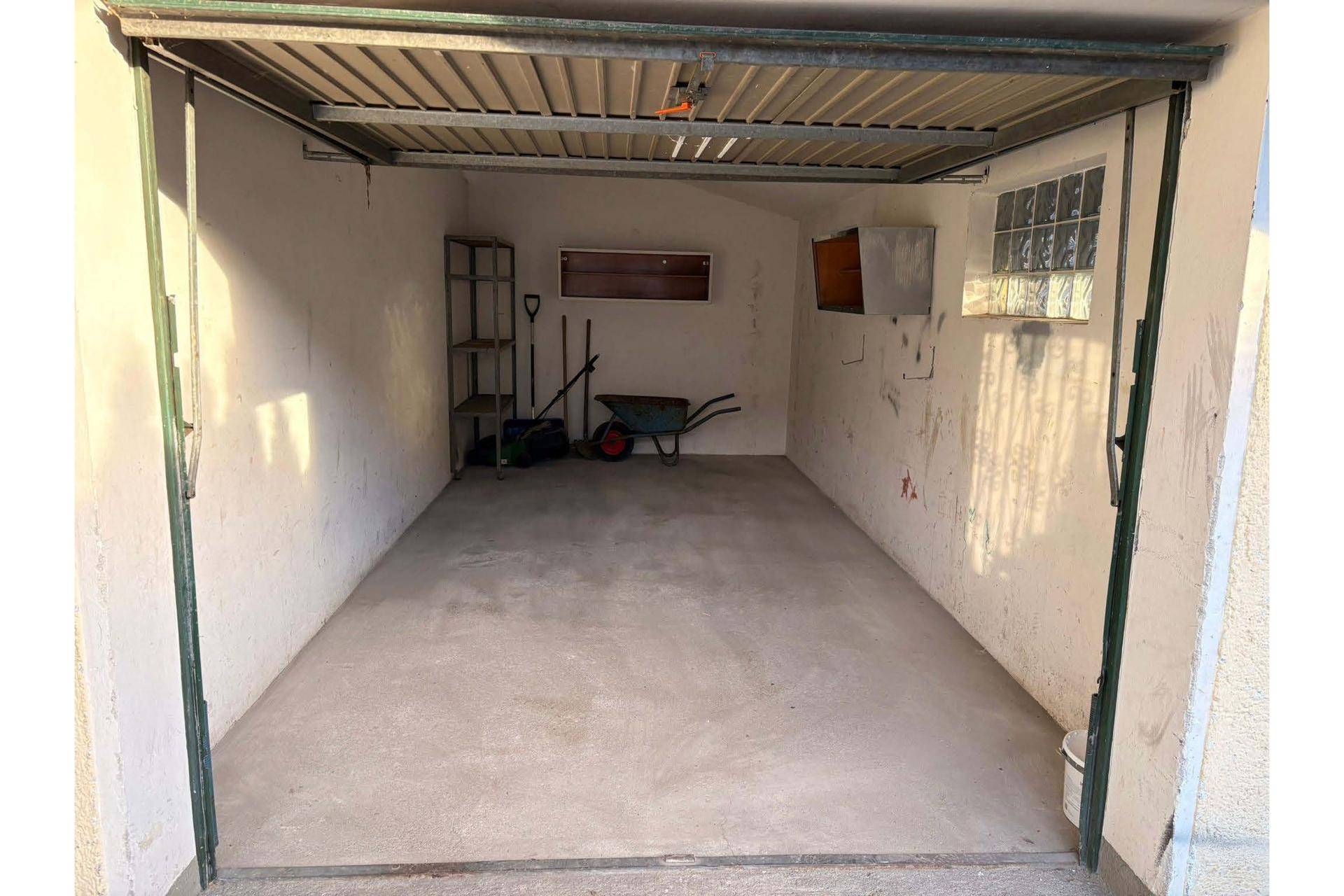 Geräumige Einzelgarage mit Betonboden und Stauraum für Werkzeuge.