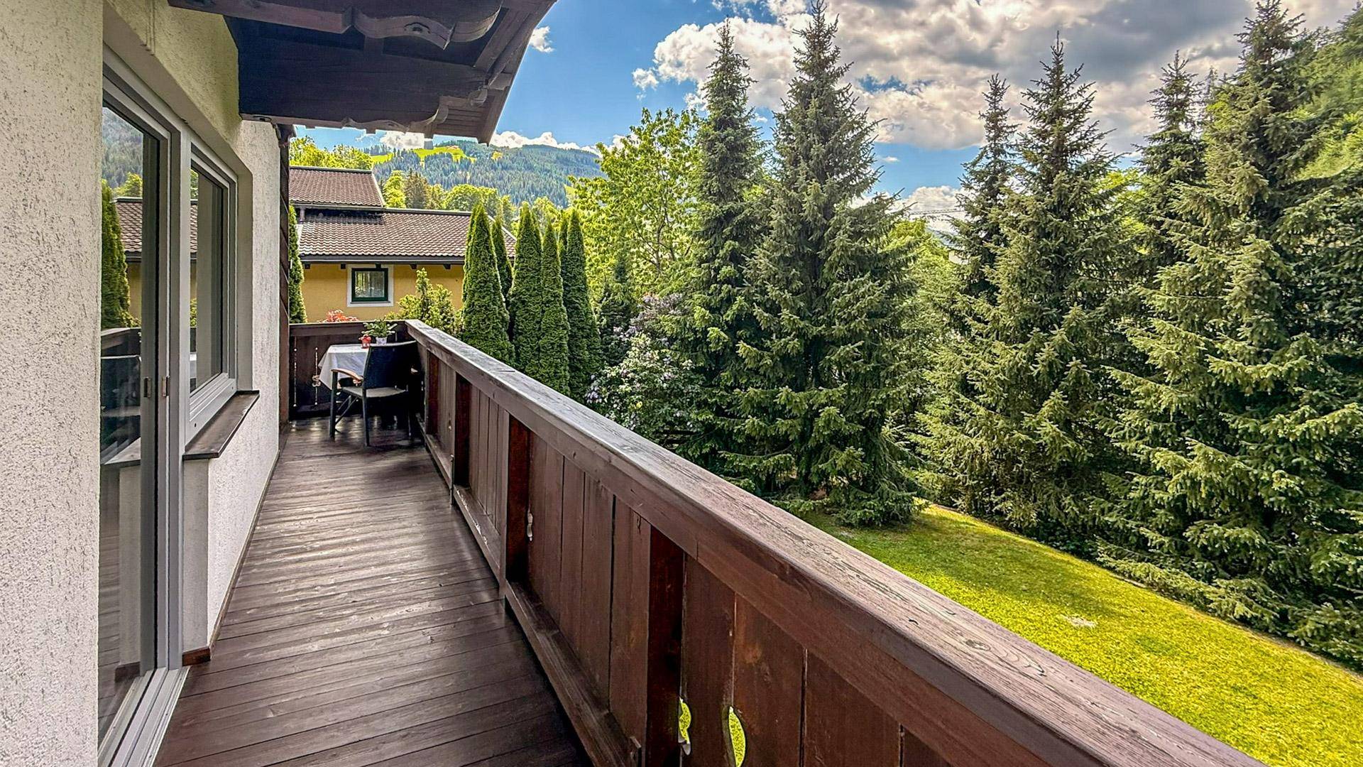 Langer Holzbalkon mit weitem Blick ins Grüne und auf die umliegende Berglandschaft.