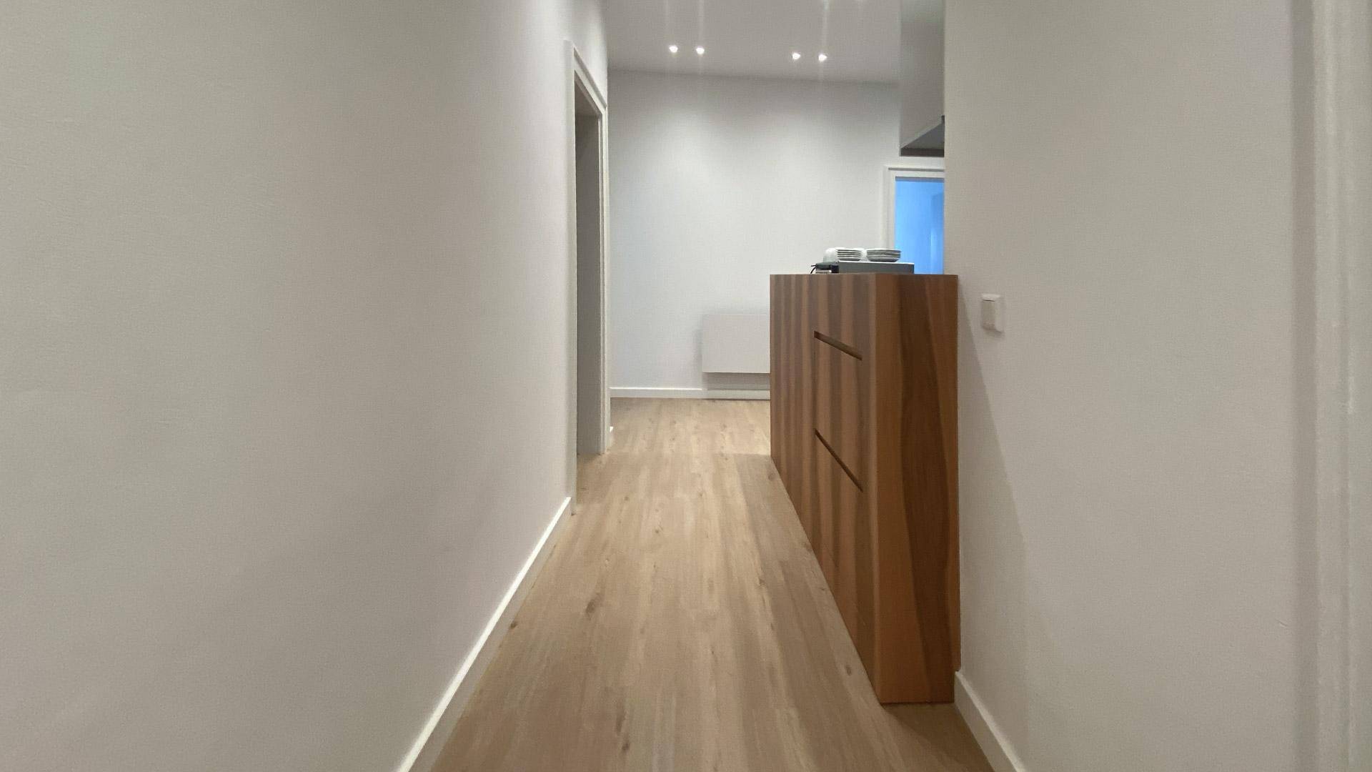 Heller Flur mit Holzboden und einer modernen Holzkommode an der Wand.