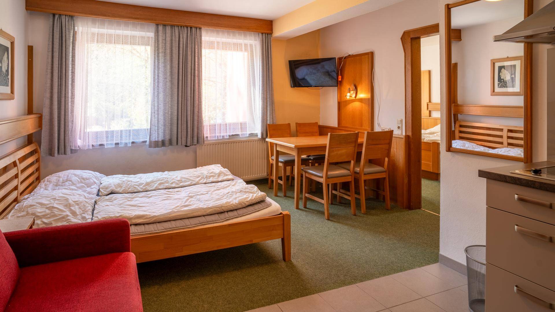 Geräumiges Schlafzimmer mit Doppelbett, Esstisch und Zugang zu einer kleinen Küchenzeile.