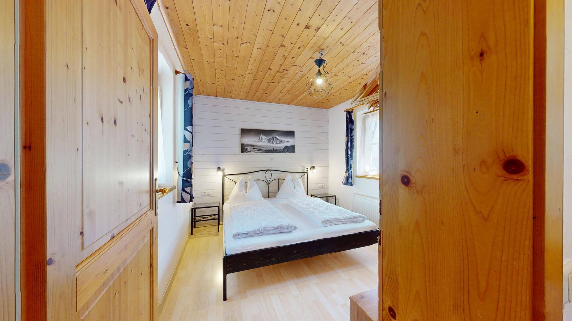 Gemütliches Schlafzimmer mit Doppelbett, Holzbalkendecke und hellem Holzboden.