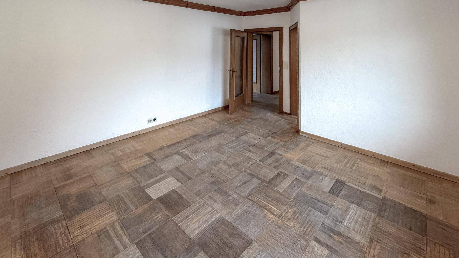 Leeres Zimmer mit Parkettboden und weißen Wänden, bereit zur individuellen Gestaltung.