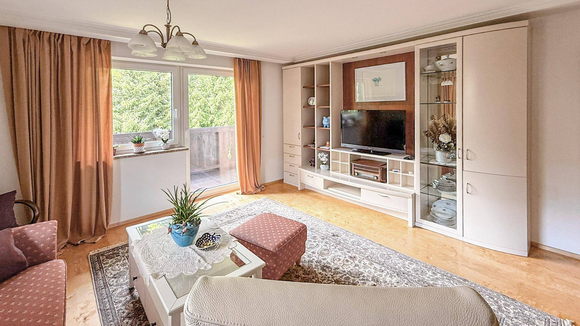 Helles Wohnzimmer mit Zugang zum Balkon, großem TV-Möbel und gemütlicher Einrichtung.