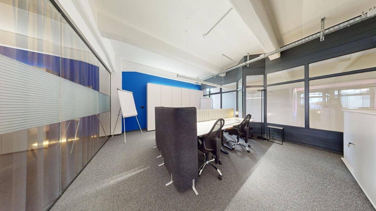 Modernes Büro mit mehreren Arbeitsplätzen, einer blauen Akzentwand und großen Fenstern, die viel Licht hereinlassen.