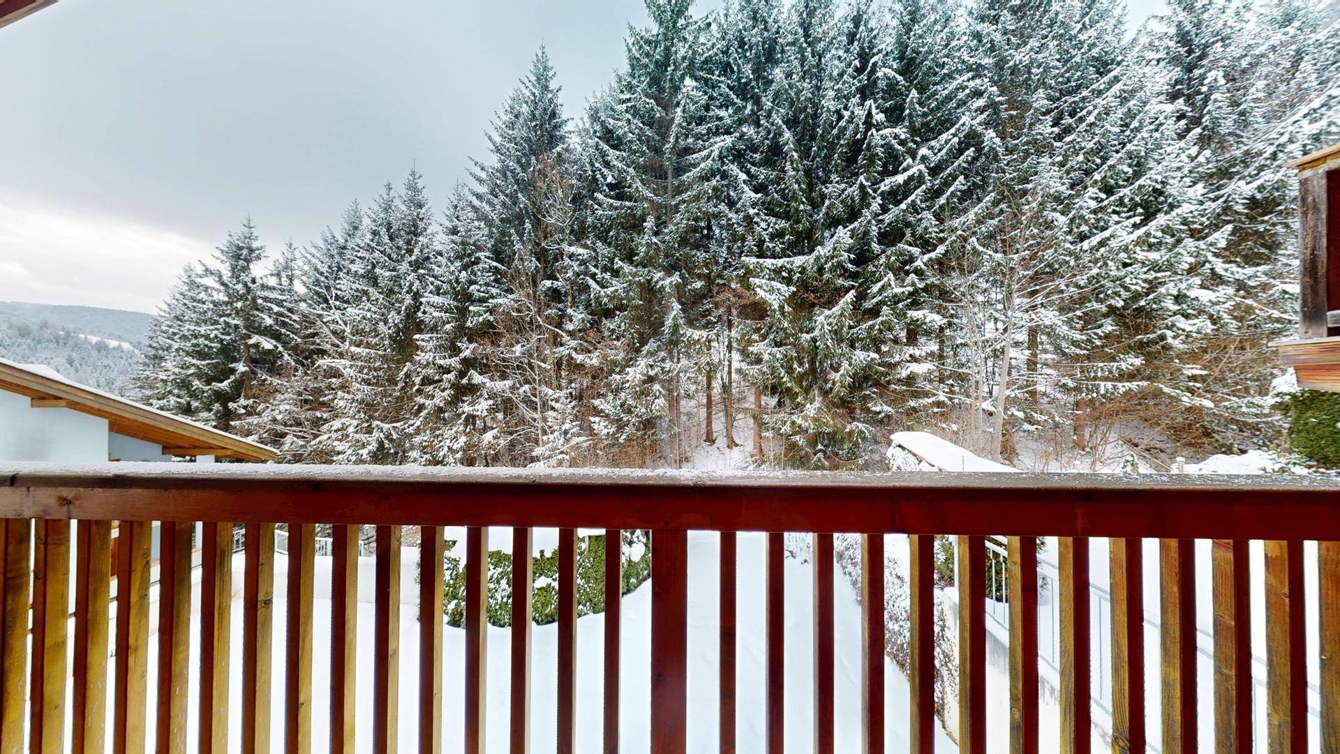 Balkon mit Holzgeländer und Blick auf verschneite Tannenbäume und die Winterlandschaft.