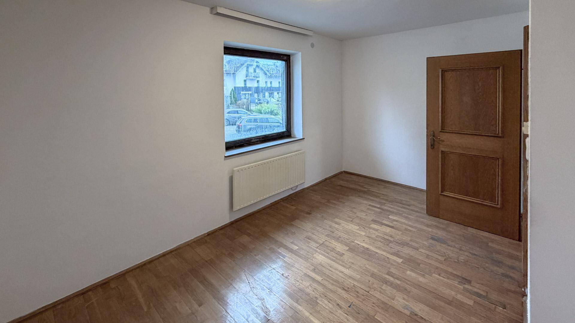 Helles Schlafzimmer mit Parkettboden, weiß gestrichenen Wänden und Fenster.