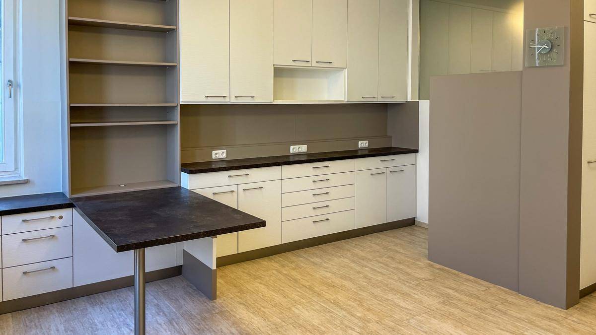 Funktionale Küche mit weißen Einbauschränken, dunkler Arbeitsplatte und einem praktischen ausklappbaren Tisch.