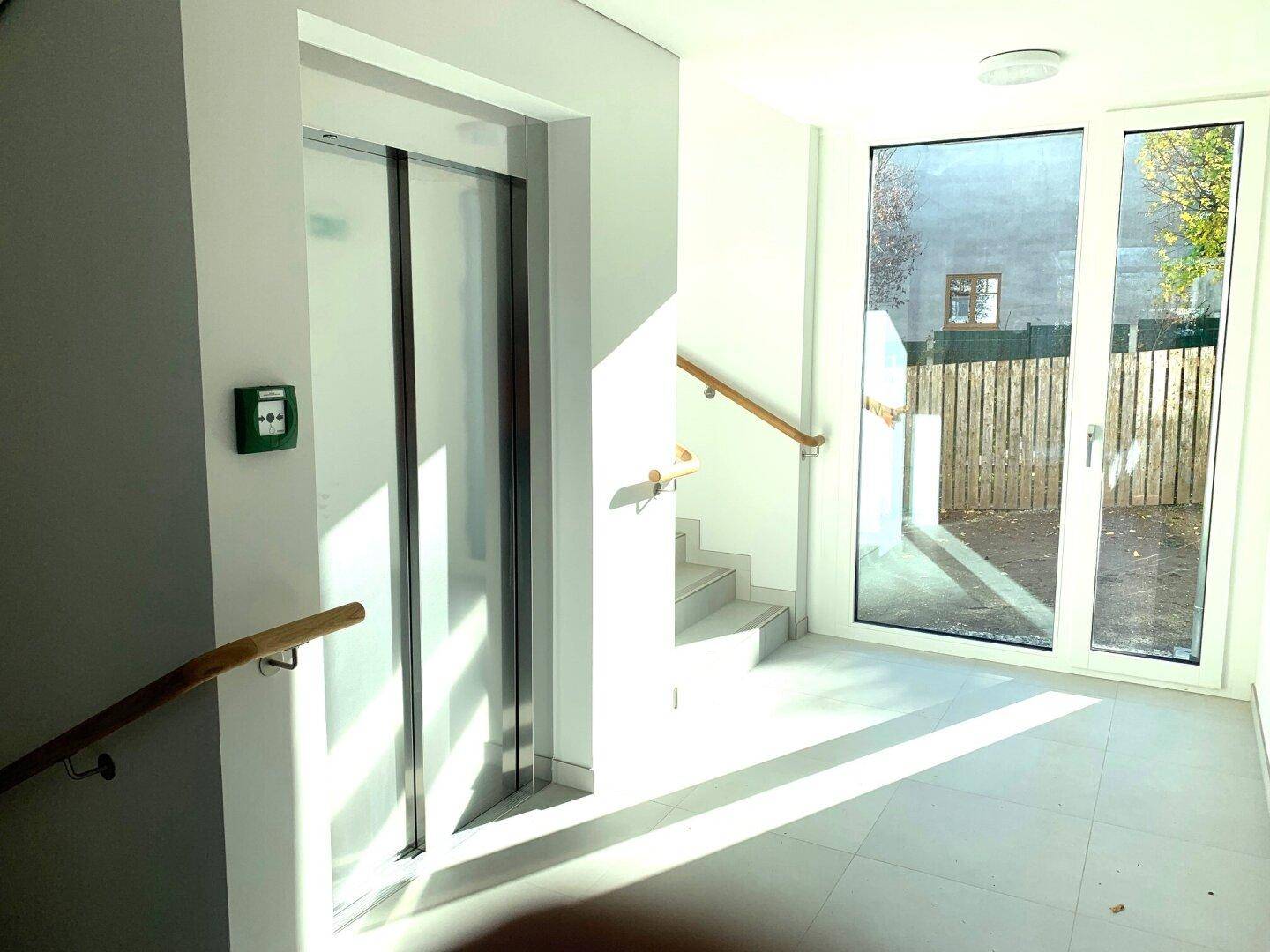 Heller Eingangsbereich mit Aufzug und Treppenhaus, das viel natürliches Licht erhält.