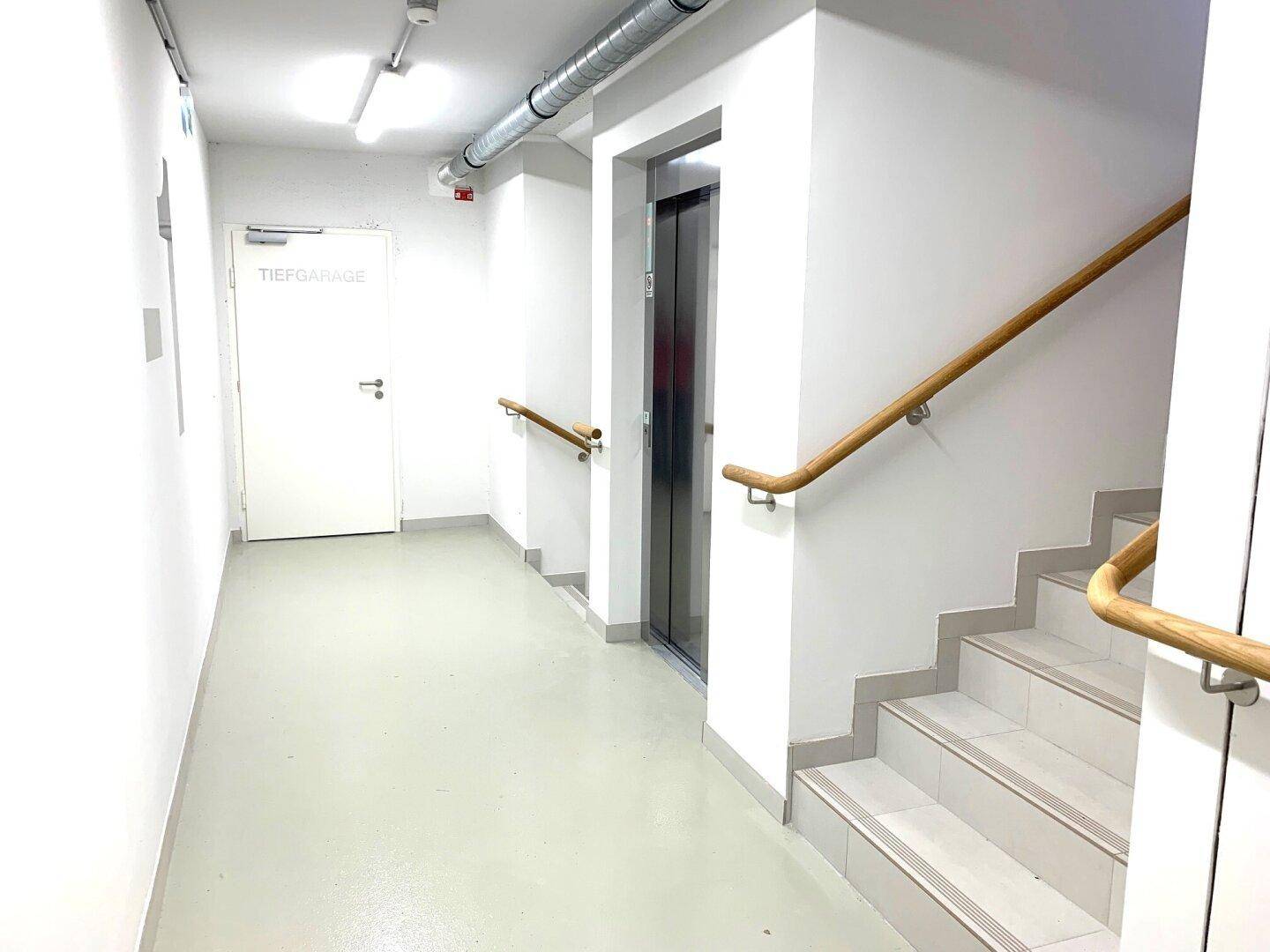 Sauberer Flur mit Aufzug und Treppenhaus, das zur Tiefgarage führt.