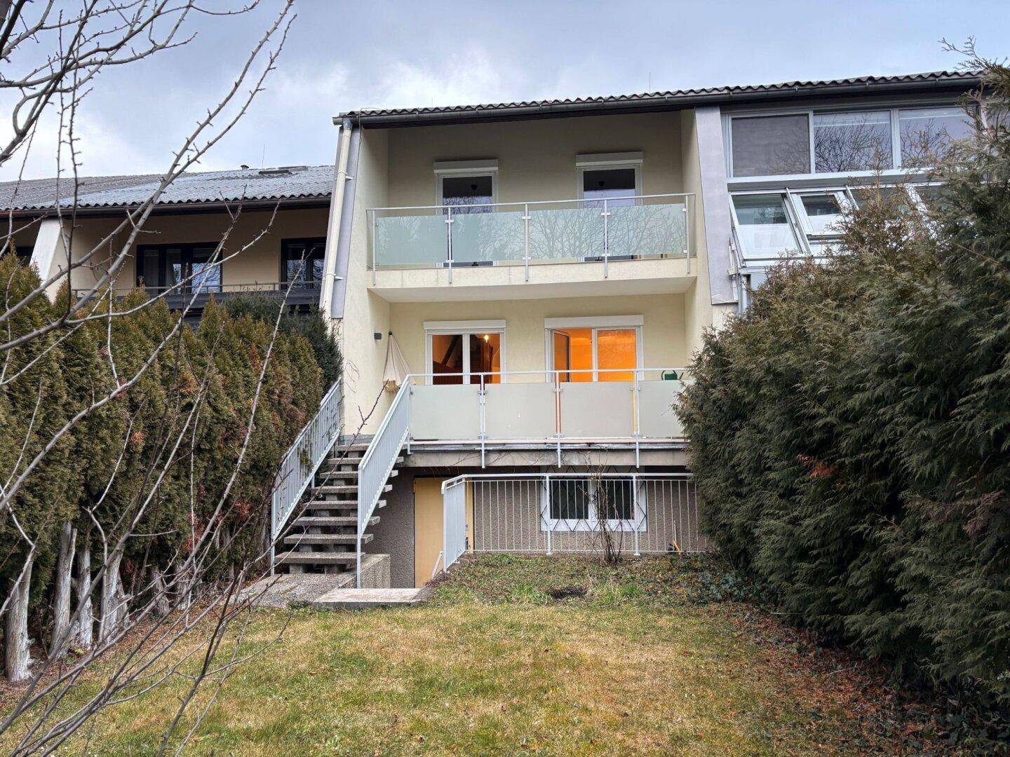 Rückseite eines Reihenhauses mit zwei Balkonen, Außentreppe und einem kleinen Gartenbereich.