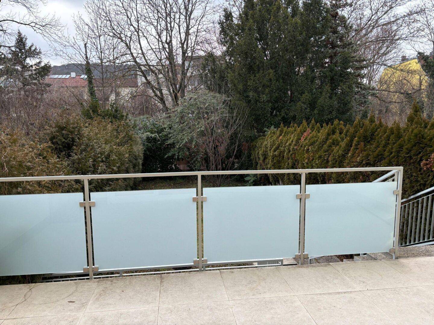 Balkon mit moderner Milchglasbrüstung und Blick auf die umliegende grüne Landschaft.