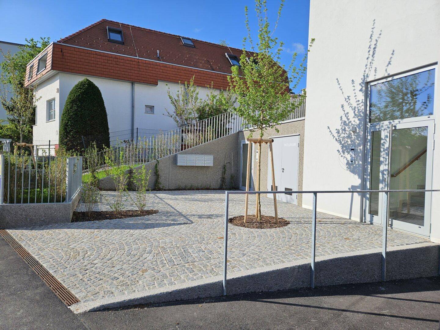 Heller Eingangsbereich mit gepflastertem Vorplatz und Zugang zum modernen Wohngebäude.