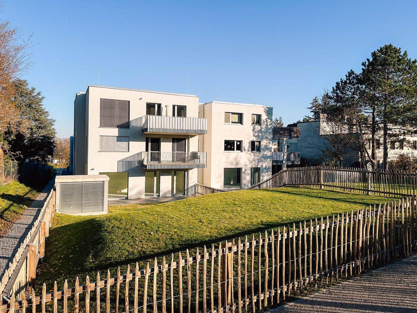 Modernes Wohngebäude mit Balkonen und Terrassen, umgeben von einer sonnigen Grünfläche.