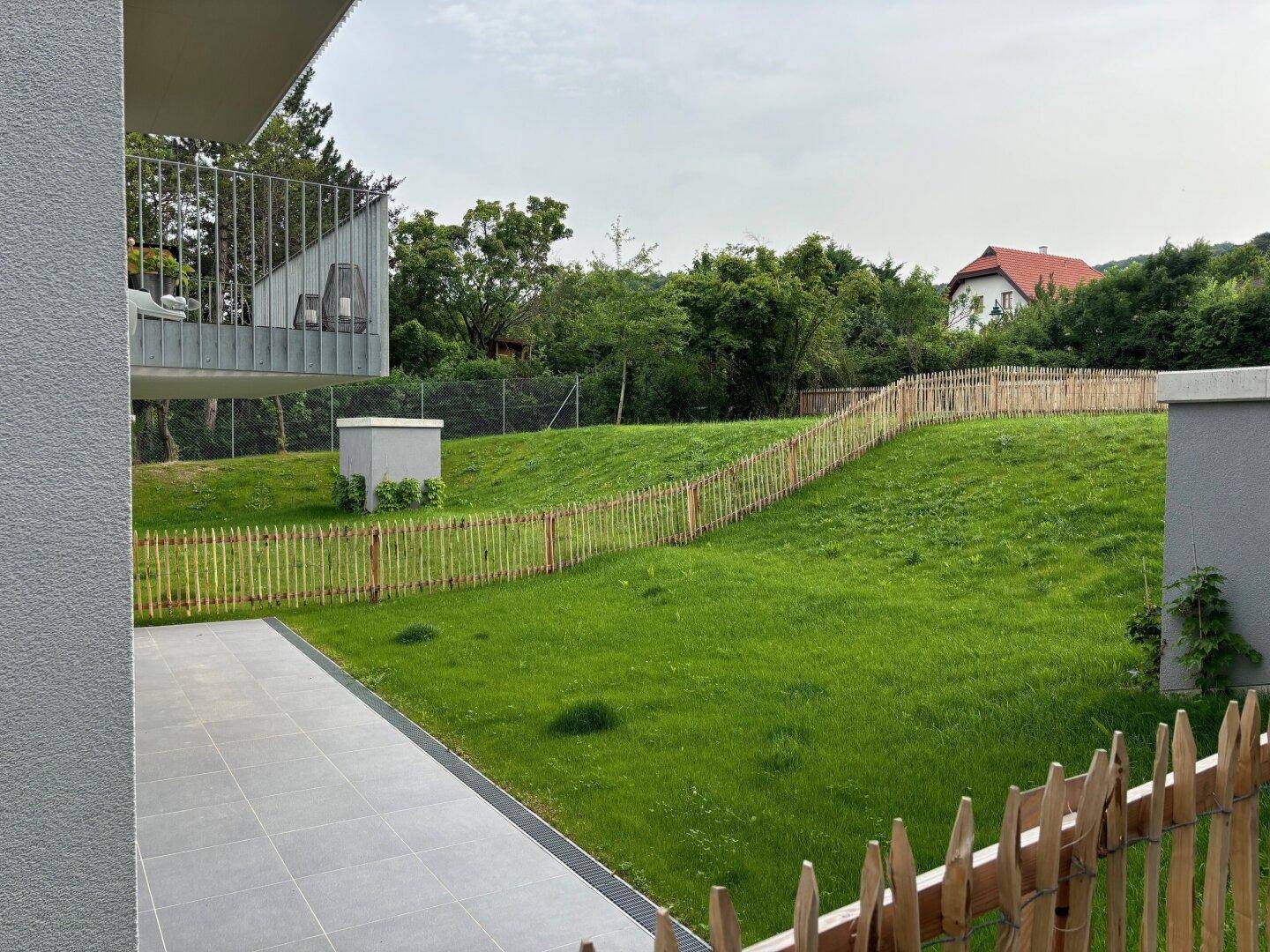 Geräumige Terrasse mit Blick auf die weitläufige, grüne Rasenfläche und die umliegende Natur.