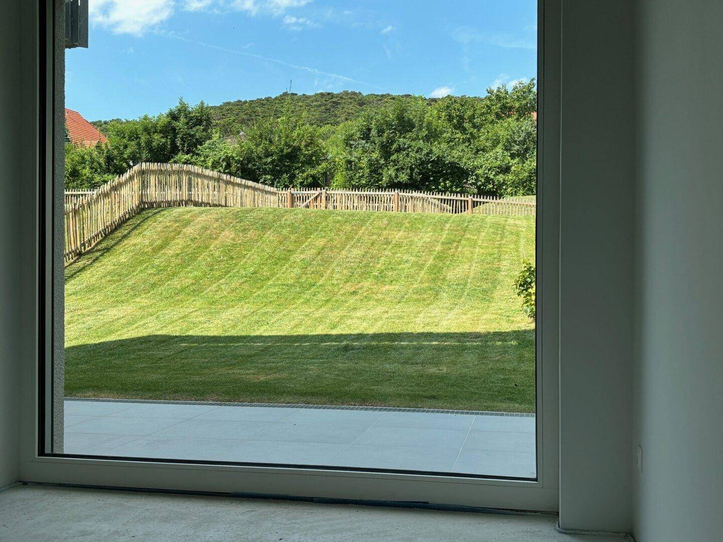 Heller Raum mit großem Fenster und Blick auf die grüne Rasenfläche und die umliegende Natur.