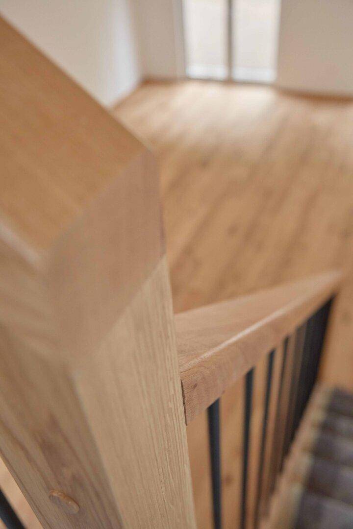 Detailaufnahme des Holzgeländers der Treppe, das die natürliche Maserung des Holzes zeigt.