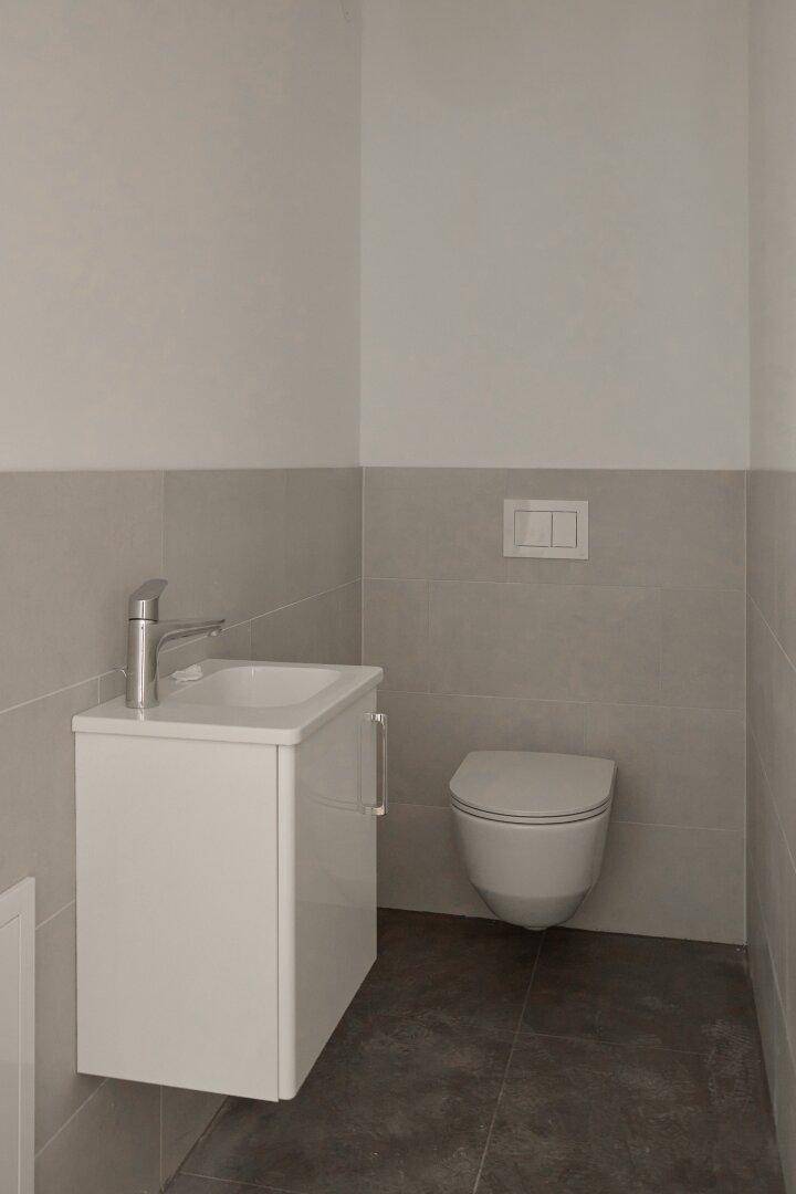 Modernes Gäste-WC mit wandhängender Toilette und kleinem Waschbecken, in hellen Tönen gehalten.