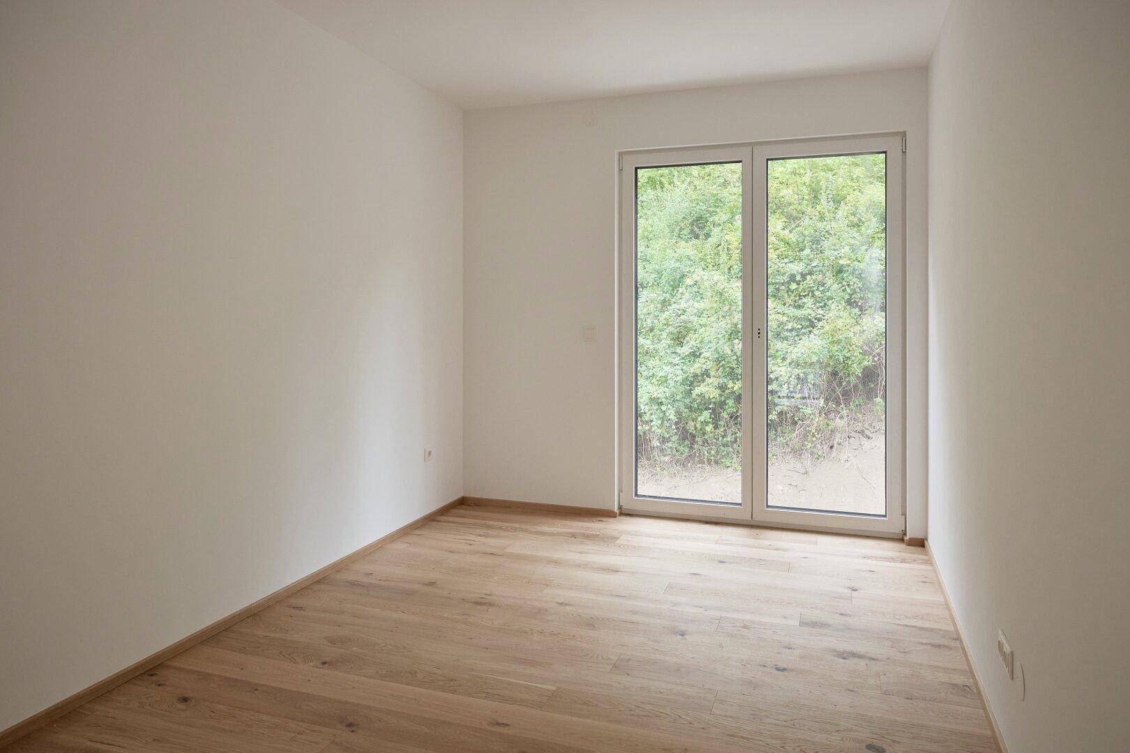Helles, unmöbliertes Zimmer mit Eichenparkett und großer Fenstertür zum Außenbereich.