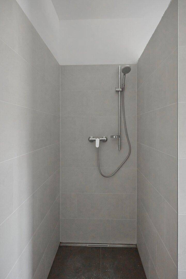 Moderner Duschbereich mit hellgrauen Fliesen und Handbrause, minimalistisch gestaltet.