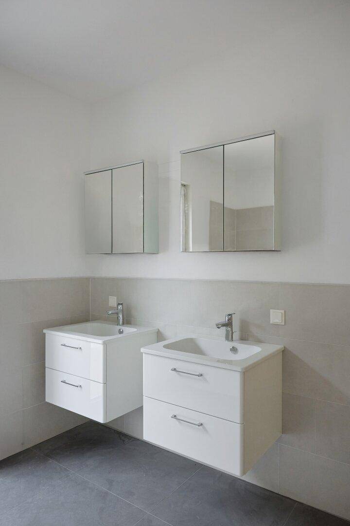Modernes Badezimmer mit zwei Waschbecken, Spiegelschränken und hellgrauen Fliesen.