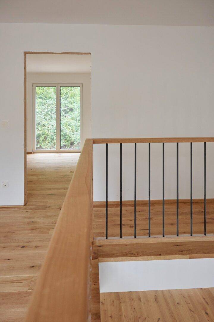 Detailansicht des Holzgeländers im Obergeschoss mit Blick auf den darunterliegenden Raum.