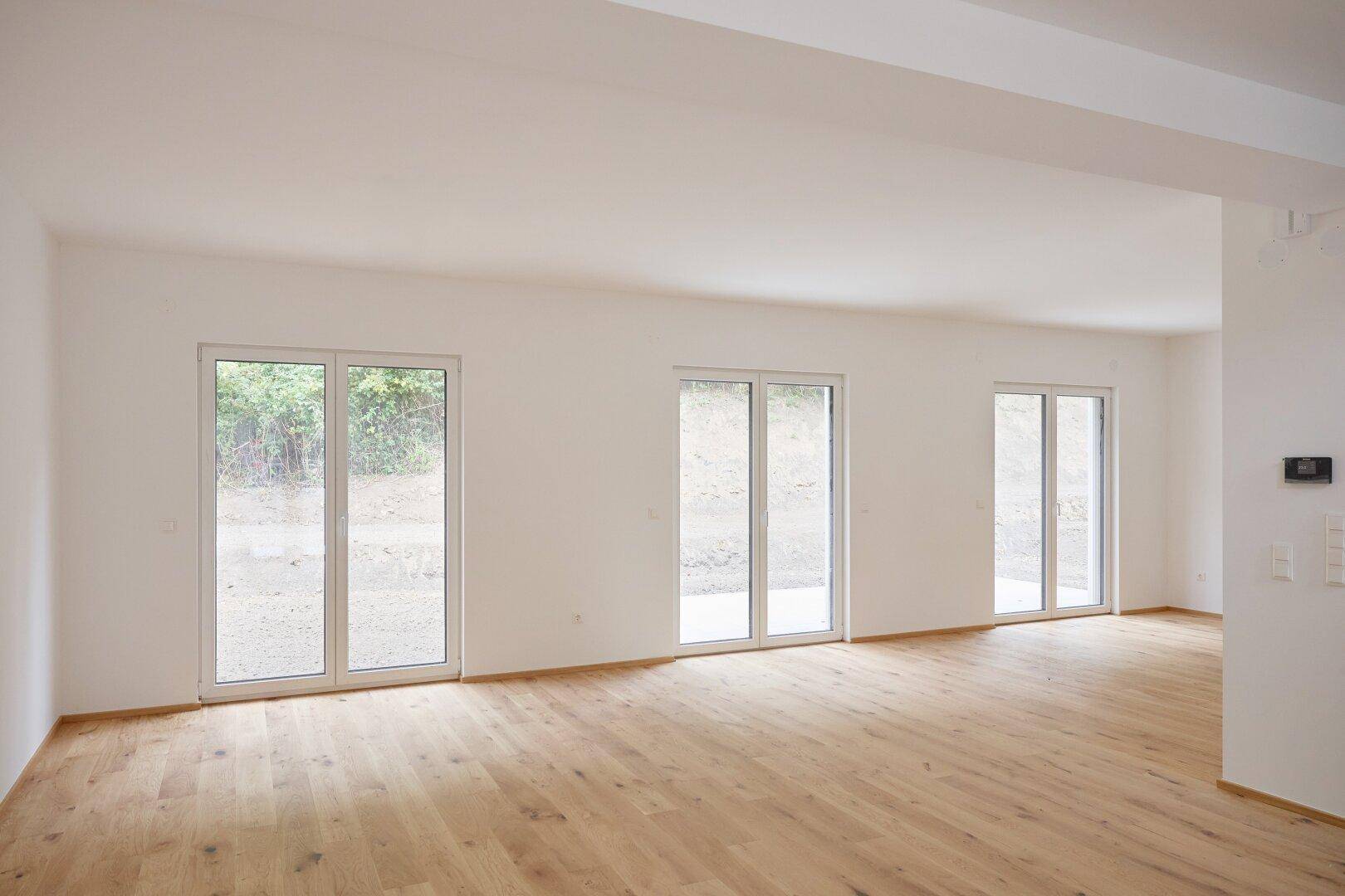 Helles, leeres Wohnzimmer mit großen Fenstertüren und neuem Eichenparkettboden.