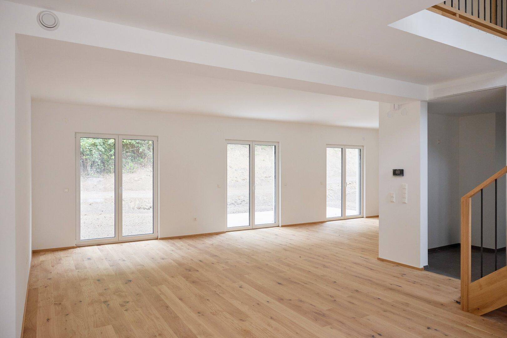 Geräumiges Wohnzimmer mit Holzboden und Blick auf die offene Treppe zum Obergeschoss.