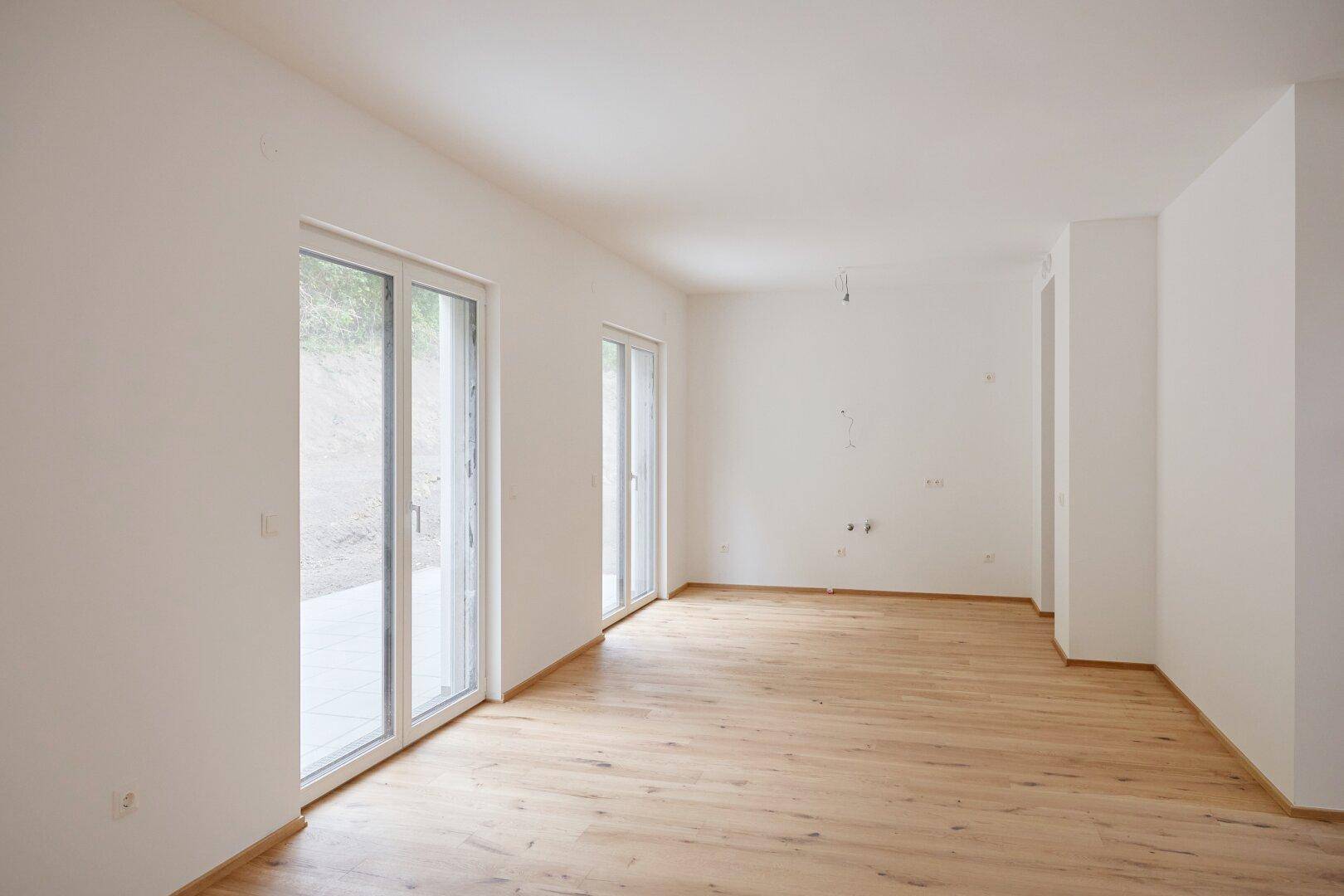 Leerer Wohnraum mit Eichenparkett und großen Fenstern, die viel Tageslicht hereinlassen.