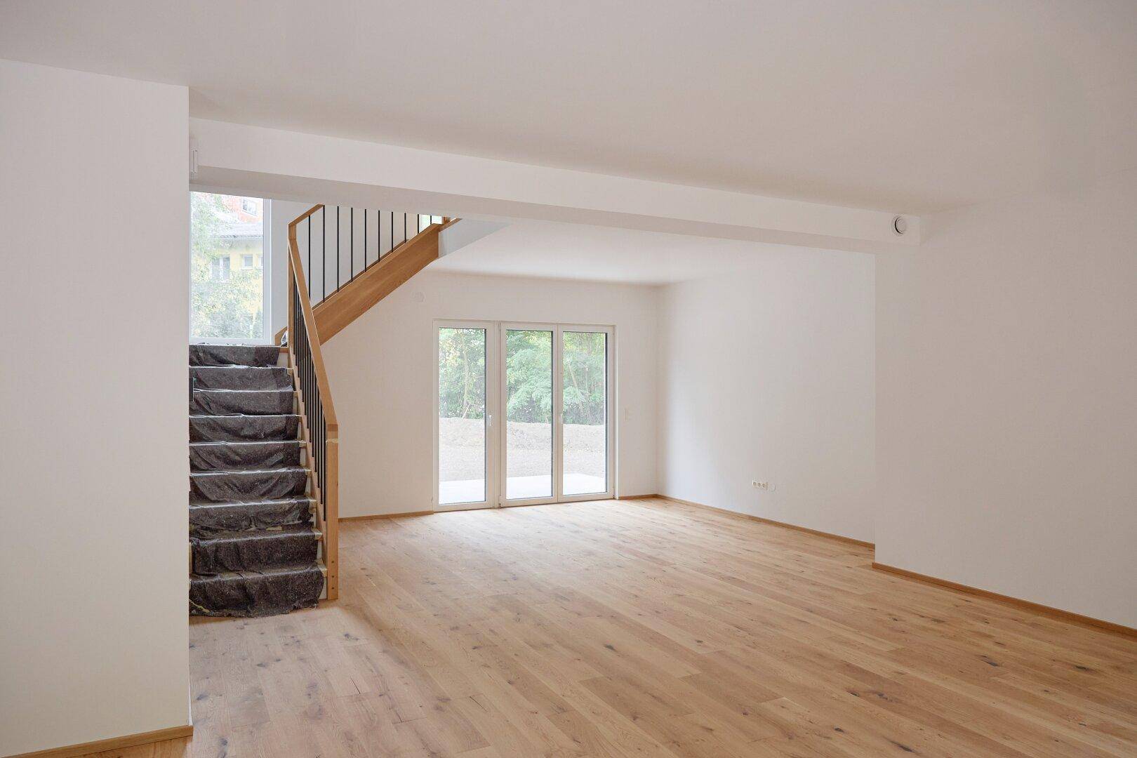 Heller Wohnbereich mit Eichenparkett und einer modernen Holztreppe, die noch abgedeckt ist.