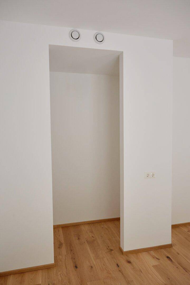 Leere Nische mit Lüftungsöffnungen und hellem Holzboden, ideal für Stauraum.