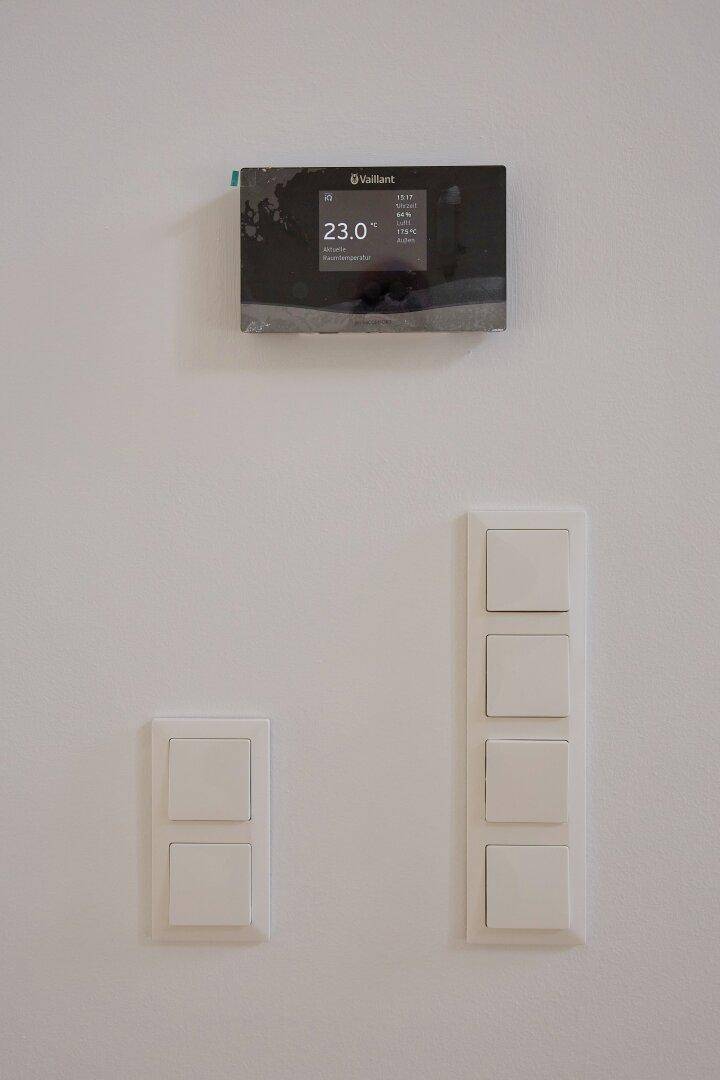 Wandmontierter Thermostat und Lichtschalter in einem modernen Innenraum.