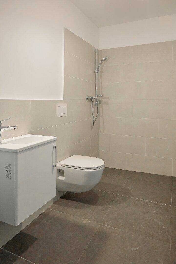 Modernes Gäste-WC mit Dusche, wandhängender Toilette und kleinem Waschbecken.