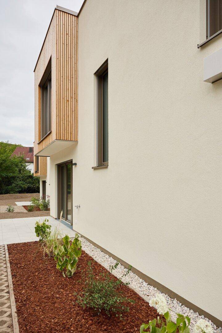 Seitenansicht des Hauses mit heller Fassade, schmalen Fenstern und neu angelegten Beeten.