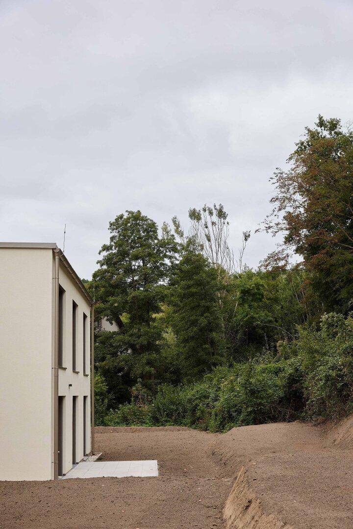 Seitenansicht eines modernen Hauses mit unfertigem Gartenbereich und bewaldetem Hang.