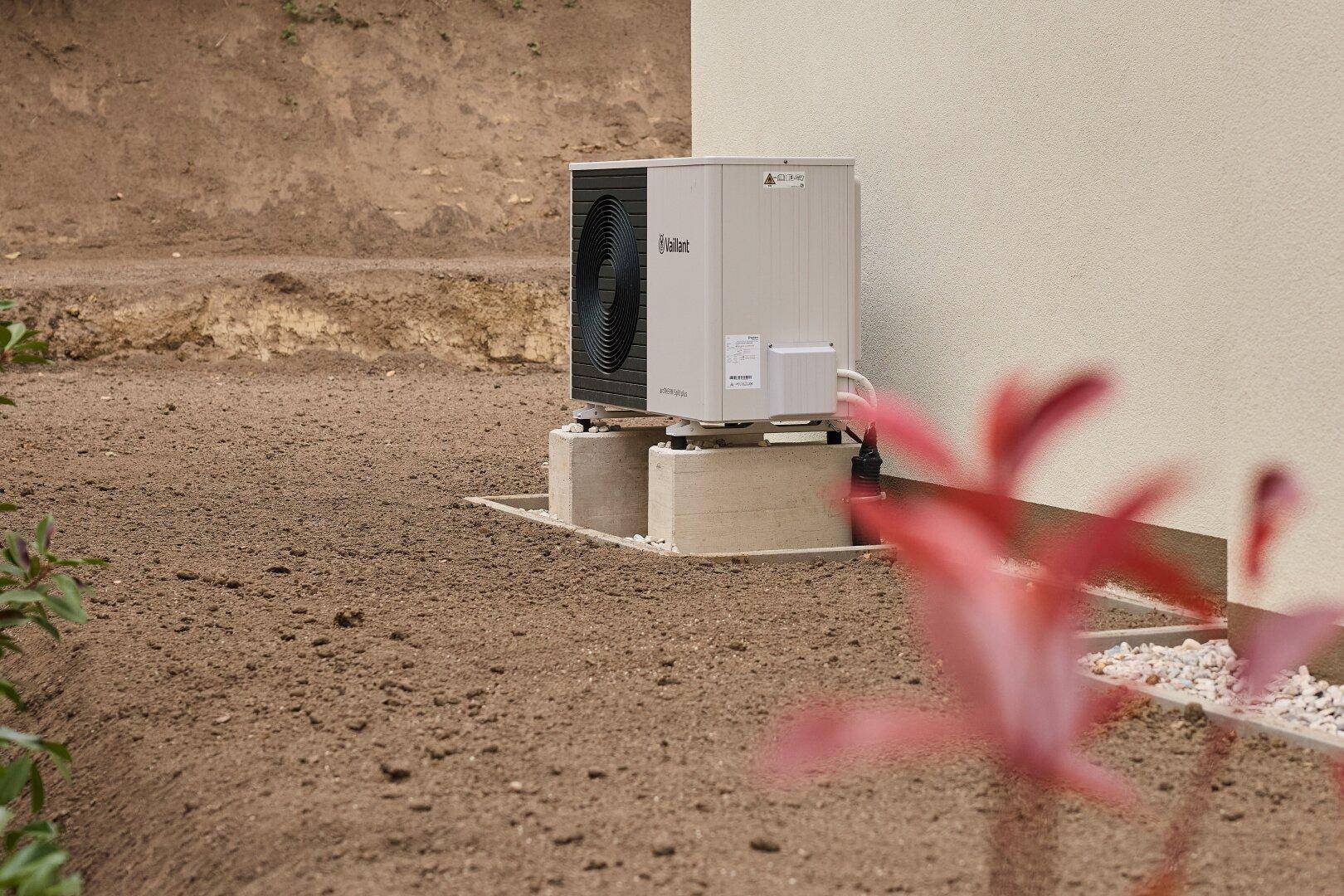 Außenansicht einer modernen Wärmepumpe auf einem Sockel neben dem Haus.
